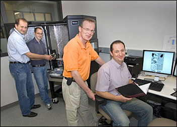 (From left) Dmytro Nykypanchuk and Mathew Maye load a sample into an atomic force microscope while Daniel van der Lelie and Oleg Gang review data at Brookhaven Labs Center for Functional Nanomaterials.