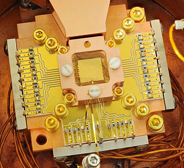 NIST physicists used this apparatus to coax two beryllium ions (electrically charged atoms) into swapping the smallest measurable units of energy back and forth, a technique that may simplify information processing in a quantum computer. The ions are trapped about 40 micrometers apart above the square gold chip in the center. The chip is surrounded by a copper enclosure and gold wire mesh to prevent buildup of static charge.
Credit: Y. Colombe/NIST