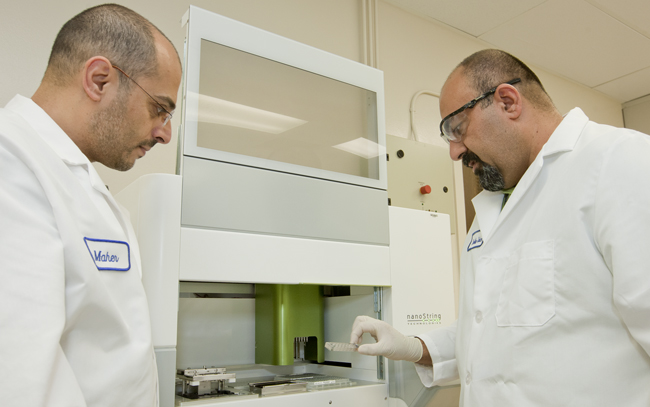 Pejman Naraghi-Arani, right, holds one of the assay chips that the Nanostring nCounter uses for detection and quantitation of RNA molecules as Maher El Sheikh looks on.
Photos by Jacqueline McBride/PAO