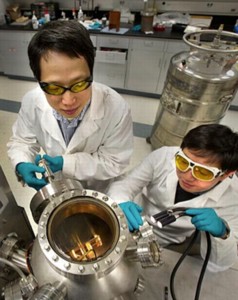 Brookhaven physicists Weidong Si (left) and Qiang Li look into the vacuum chamber where the new high-field iron-based superconductors are made through a process called pulsed-laser deposition.
