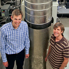 NIST physicist and JILA Fellow Konrad Lehnert (left) and post-doctoral researcher Tauno Palomaki in the JILA laboratory where they entangled a microscopic mechanical drum with electrical signals. The micro-drum, just 15 micrometers in diameter and 100 nanometers thick, is chilled and manipulated inside the tall tank.
Credit: Baxley/JILA