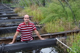 Nanotechnology researcher Lee Ferguson stands amid a collection of simulated wetlands called mescosms at Duke University. Each wetland-in-a-box is used to run the experiment under varying conditions.
