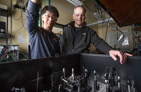 NREL scientists Ye Yang and Matt Beard stand in front of a transient absorption spectrometer in their laser lab.