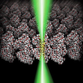 A schematic showing a focused electron beam (green) shining through a polymeric film (grey: carbon atoms; red: oxygen atoms; white: hydrogen atoms). The glowing area (yellow) indicates the molecular volume chemically modified by the focused electron beam.