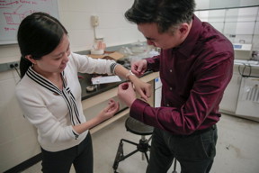 Materials science and engineering professor Xudon Wang fits a new wound dressing around the wrist of graduate student Yin Long. The device stimulates healing using electricity generated from the body's natural motions.

CREDIT
UW-Madison photo by Sam Million-Weaver