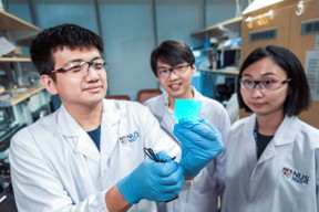 The  NUS  research  team  behind  the  novel  electronic  material  is  led  by  Assistant  Professor Benjamin  Tee  (centre).  With  him  are  two  team  members:  Mr  Wang  Guanxiang  (left),  who  is holding a sample of the illuminated material, and Dr Tan Yu Jun (right).Credit:National University of Singapore
