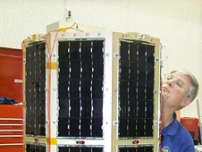 Dr. Billy R. Smith Jr., director of the USNA Small Satellite Program and MidSTAR-1 program manager, inspects MidSTAR-1 for damage after vibration testing at the Naval Research Laboratory. This test demonstrated that the satellite could survive the rigors of launch and retain functionality. High-efficiency, triple-junction gallium arsenide solar cells cover the sides; the S-band transmit antenna is visible at the upper right. The external neutron detector for the MicroDosimeter Instrument (MiDN) is visible on the top. Credit: USNA