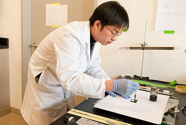 Bing Hu, a post-doctoral fellow, prepares a small square of ordinary paper to with an ink that will deposit nanotubes on the surface that can then be charged with energy to create a battery.
