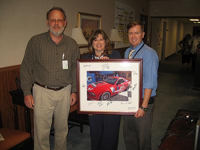 From left, Tom Erickson, chief, Reliability, Availability and Maintainability Engineering & System Assessment Division; Patti Martin, director, Engineering Directorate; and Kris Walker, RAM & SA team lead/Attack & Unmanned Aerial Systems, display a photograph of the No. 61 Roush Performance Products Ford Mustang GT autographed by the Roush-Fenway Racing Team.