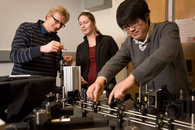 Ulrich Wiesner, left, works with graduate students Jennifer Drewes and Kai Ma to characterize the size and brightness of C dots in their Bard Hall lab. Credit Jason Koski/University Photography