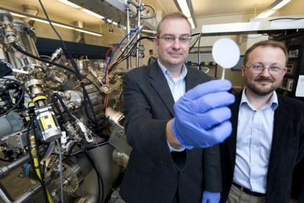 Purdue professors Michael Manfra, from left, and Gabor Csathy stand next to the high-mobility gallium-arsenide molecular beam epitaxy system at the Birck Nanotechnology Center. Manfra holds a gallium-arsenide wafer on which his research team grows ultrapure gallium arsenide semiconductor crystals to observe new electron ground states that could have applications in high-speed quantum computing. (Purdue University photo/Andrew Hancock)