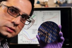 Georgia Tech postdoctoral fellow Hossein Sojoudi holds a wafer containing graphene p-n junctions, while the screen display in the background shows electrical data measured in the devices. (Credit: Gary Meek)