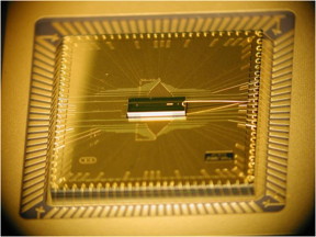 A photograph of the completed BGA trap assembly. The trap chip is at the center, sitting atop the larger interposer chip that fans out the wiring. The trap chip surface area is 1mm x 3mm, while the interposer is roughly 1 cm square.
CREDIT: D. Youngner, Honeywell