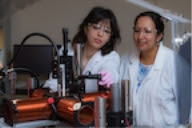 Rice University graduate student Elaa Hilou (left) and Professor Sibani Lisa Biswal set up an experiment in a device that combines a rotating magnetic field and a microscope. The researchers are studying the effects of a spinning field on magnetic particles. Their findings could help researchers model colloids for cosmetics as well as catalysts for chemicals, among other applications, in a physical system. (Credit: Jeff Fitlow/Rice University)

