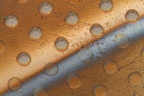 This photo shows circles on a graphene sheet where the sheet is draped over an array of round posts, creating stresses that will cause these discs to separate from the sheet. The gray bar across the sheet is liquid being used to lift the discs from the surface.

Image: Felice Frankel